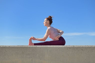 Açık havada yoga yapan sağlıklı bir kadının portresi. Güneşli bir günde arka planda mavi gökyüzü olan bir kadın asana çalışıyor.