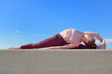 Açık havada yoga yapan sağlıklı bir kadının portresi. Güneşli bir günde arka planda mavi gökyüzü olan bir kadın asana çalışıyor.