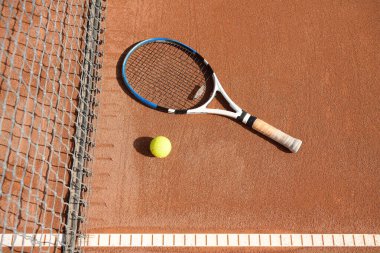 Tenis topu ve raket kil tenis kortunda, ağların yanında ve güneşli bir günde çizgi üzerinde. Eşleşme yok