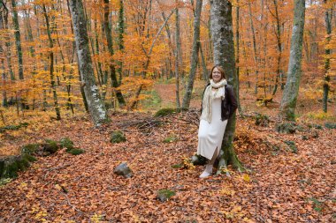 Sonbaharda kayın ormanındaki bir kadın ağaç gövdesine yaslanmış kameraya bakıyor.