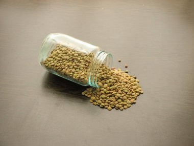  Kurutulmuş yeşil mercimek kahverengi ahşap yüzeyde bir cam kavanozdan dökülür. Ahşap masada cam bir kavanozda yeşil mercimek. Cam bir tabak içinde yeşil mercimek. Ahşap arka plan