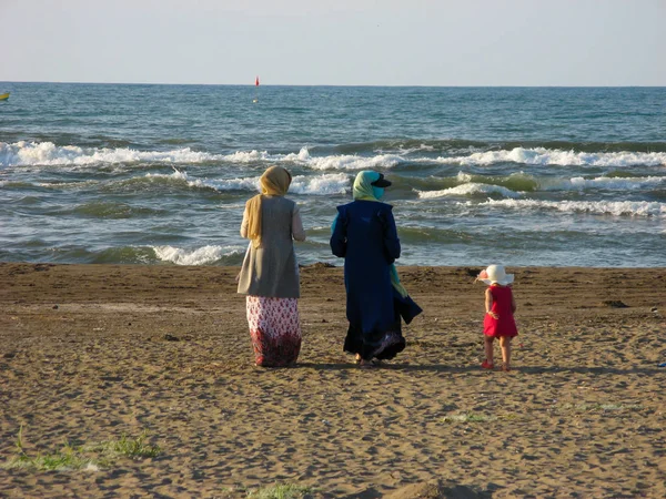 Müslüman kadınlar bantüre yürüyüş plaj. İran'da Hazar Denizi sahilinde yürüyen türbanlı Müslüman kadınlar, Anzali. Sahilde küçük bir kızla müslüman kadınlar. Arkadan görüntüle. 