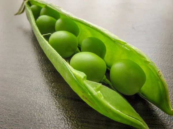 Green pea pod dark peas. Closeup of fresh green peas (Pisum sativum) in a glass jar on a wooden table.  Green peas in a glass dish on a dark background.