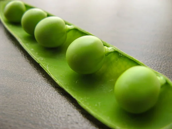 Green pea pod green peas. Closeup of fresh green peas (Pisum sativum) in a glass jar on a wooden table.  Green peas in a glass dish on a dark background.