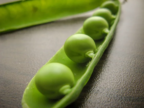 Green pea pod green peas. Closeup of fresh green peas (Pisum sativum) in a glass jar on a wooden table.  Green peas in a glass dish on a dark background.