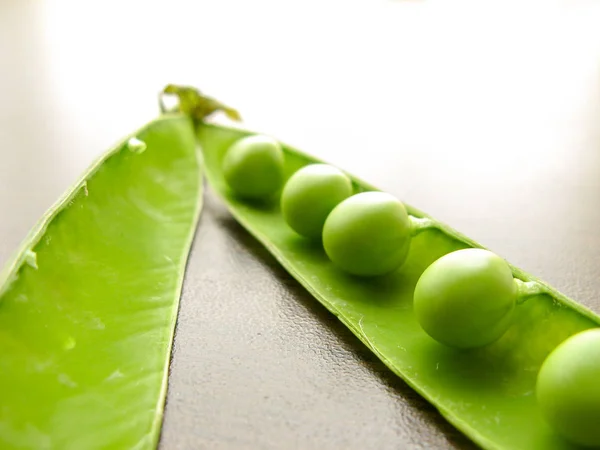 Green pea pod green peas. Closeup of fresh green peas (Pisum sativum) in a glass jar on a wooden table.  Green peas in a glass dish on a dark background.