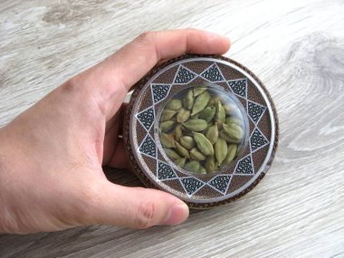 mashhad, IRAN, 01 03 2020: Green cardamom pods into handcraft box on wooden background. Hand on box. Close up.