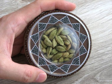 Mashhad, IRAN, 01 03 2020: Close up of green cardamom pods into handcraft box on wooden background. Hand on box. 