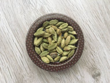 Ahşap masadaki kapta kurumuş organik kakule kapsülleri, yakın çekim ve üst manzara..