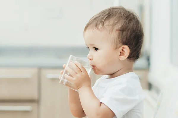 A boy drinks water in the kitchen
