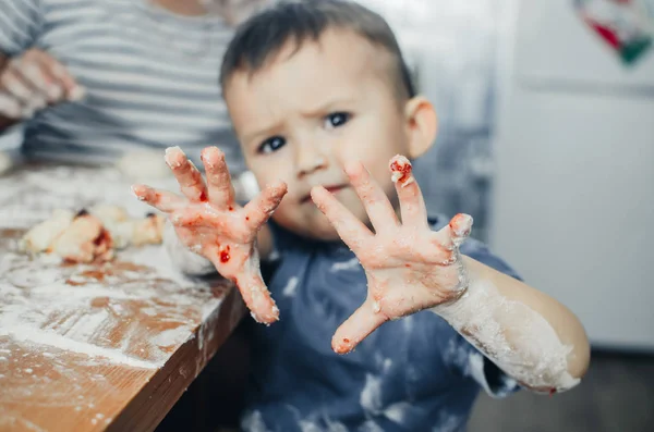 baby in the kitchen shows dirty hands in flour and dough