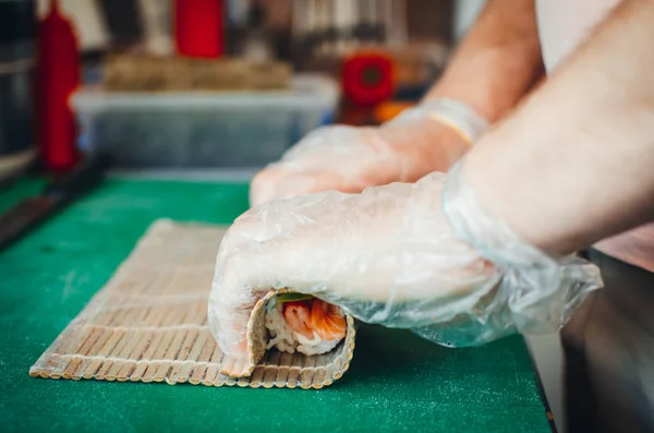 Cook making a sushi roll with bamboo mat. Chef sat professional kitchen preparing sushi. The process of sushi roll preparation.