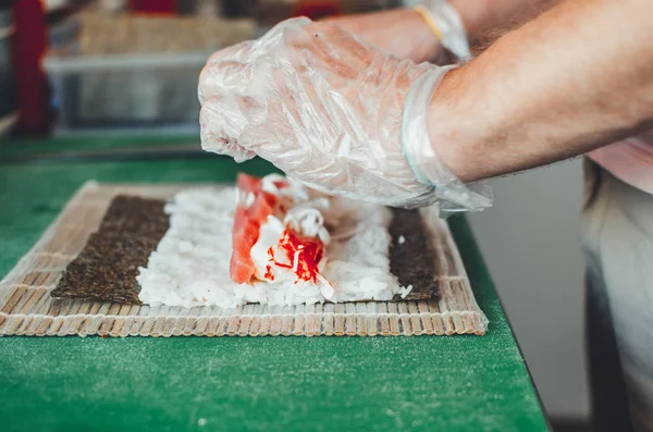 Cook making a sushi roll with bamboo mat. Chef sat professional kitchen preparing sushi. The process of sushi roll preparation.