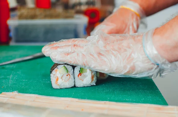 The cook makes a sushi roll with bamboo Mat cuts. The process of cooking sushi roll