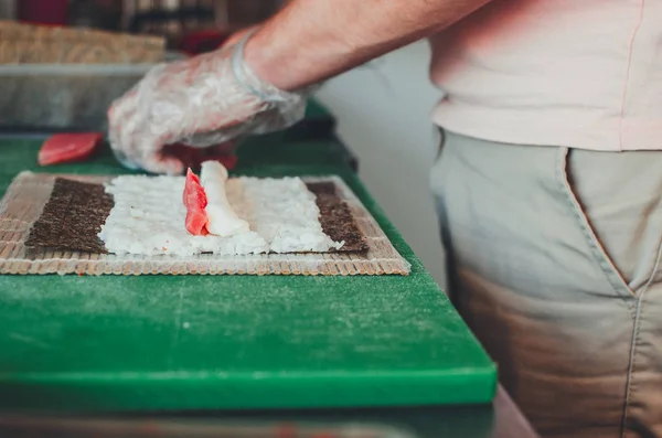 The cook makes a sushi roll with bamboo Mat cuts. The process of cooking sushi roll