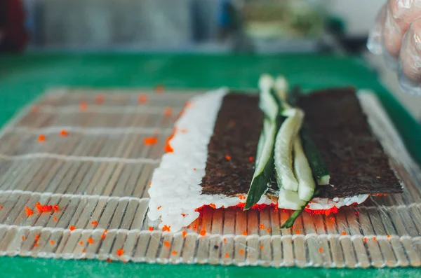 The cook makes a sushi roll with bamboo Mat cuts. The process of cooking sushi roll