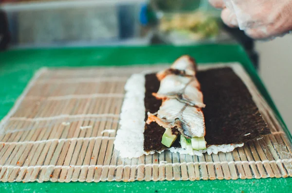 The cook makes a sushi roll with bamboo Mat cuts. The process of cooking sushi roll