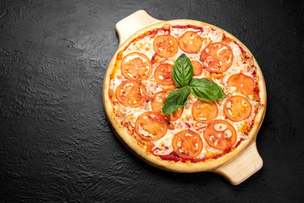 Pizza MARGARITA on a black background, tomato-based with mozzarella, Basil, parsley and tomatoes on a wooden stand