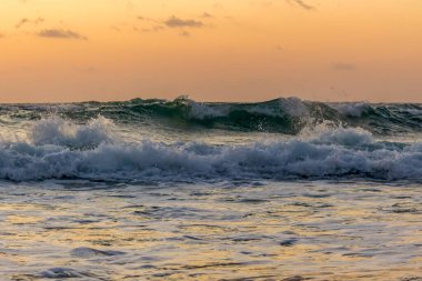 Gün batımında denizde dalgalar. Ön planda, güneş ışınları suya yansıyor..