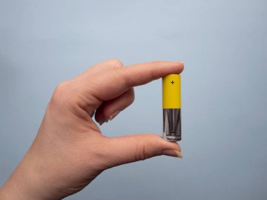 Kadın eli, mavi arka planda gümüş ve sarı Aa büyüklüğünde bir batarya tutuyor..