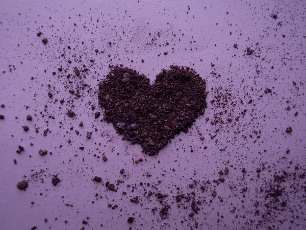 Crushed dark plum shimmer eyeshadows in heart shape scattered on dirty purple background.