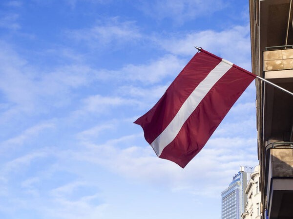 Latvian flag hanging on a building waving in the wind against a blue sky on a sunny day. 2020-01-04. Riga, Latvia. 