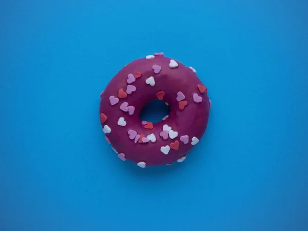 Fotokopi alanı olan mavi bir arka plan manzarasında izole edilmiş jöleli kalplerle süslenmiş pembe çörek. Tatlı Sevgililer Günü konsepti.