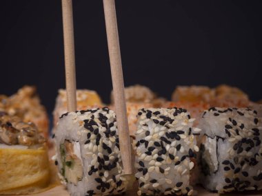 Sushi dürümlerinden birini ahşap çubuklarla kapatıyoruz. Teriyaki somonlu suşi, krem peynir, tamago omleti, yengeç kremi, avokado ve susam tohumlu. Japon mutfağı.. 