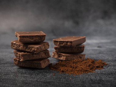 Kırık çikolata parçalarına kahve tozu serpiştirilmiş. Gri taştan arka plana yakın..