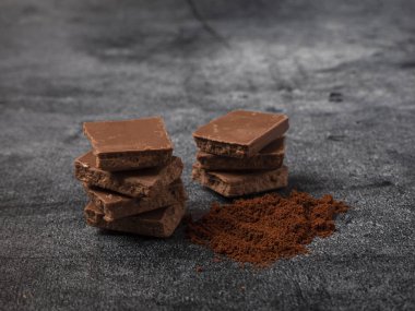 Kırık çikolata parçalarına kahve tozu serpiştirilmiş. Gri taştan arka plana yakın..