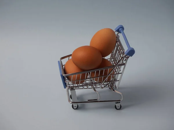 Mini shopping trolley filled with brown eggs. Shopping cart full of eggs isolated on blue background. Put all your eggs in one basket concept.