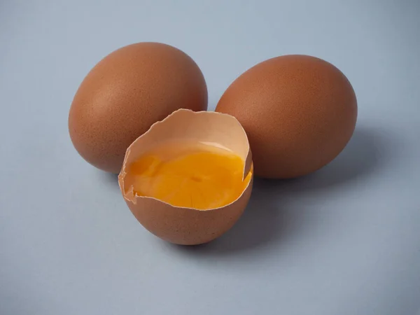 İki tam pişmemiş kahverengi tavuk yumurtası ve mavi arka planda sarı sarılı kırık yarım yumurta.. 