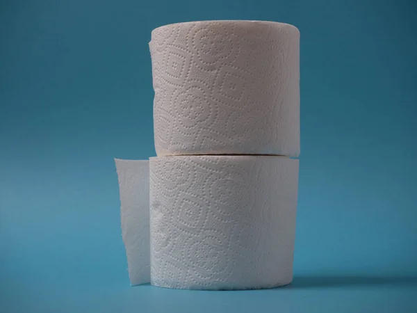 Two rolls of toilet paper stand on top of each other on a blue background close up.