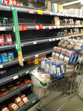 Süpermarkette bir market arabasında yarısı boş rafların yanında pirinç stokları ve diğer mısır gevrekleri var. Coronavirus COVID-19 yüzünden yemek paniği. St. Petersburg, Rusya. 2020-03-18.