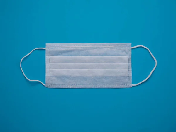 White medical face mask isolated on a blue background close up.