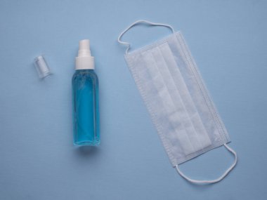 Beyaz tıbbi maske ve el dezenfektanı mavi arka planda. Coronavirus COVID-19 önleme kavramı.