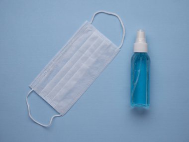 Beyaz tıbbi yüz maskesi ve antibakteriyel el dezenfektanı mavi arka plan manzaralı. Coronavirus COVID-19 önleme kavramı.