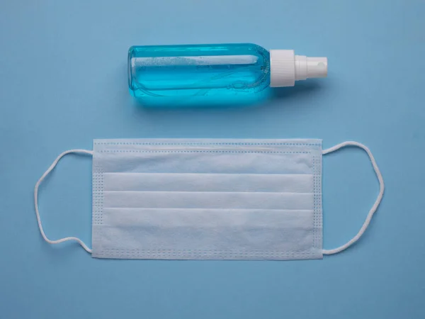 Beyaz tıbbi maske ve el dezenfektanı mavi arka planda. Coronavirus COVID-19 önleme kavramı.