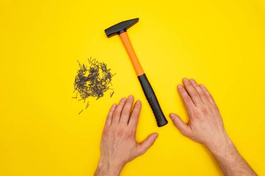 Hammer, male hands and pile of nails on yellow background
