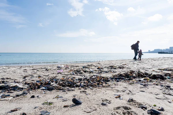 Father with his baby are walking at the trashed beach. — Stockfoto