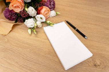 Beautiful bouquet from roses on wooden background,note book and pencil.