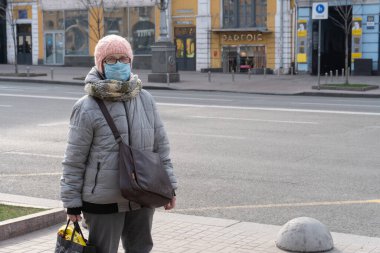 Kiev, Ukrayna, 27 Mart 2020, Yüz koruyucu maskeli yaşlı Ukraynalı kadın sokakta kalıyor
