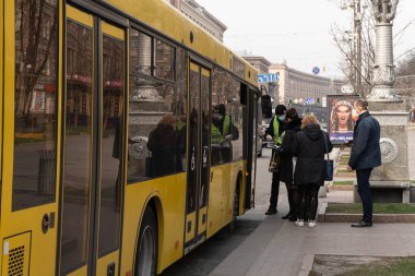 Kiev, Ukrayna, 27 Mart 2020, insanlar otobüs durağındaki otobüslerde koruyucu maskeler takıyor.,