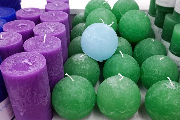 Multi-colored wax candles on a white shelf. Wax candles in the shape of a cylinder and a sphere. Candles of green, purple and blue on the shelves of the store. Romantic atmosphere and relaxation.