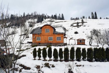 Kışın dağlarda eski ahşap bir ev. Pencereli küçük bir ev ve köyde bir ek bina. Bulutlu bir günde kış manzarası.