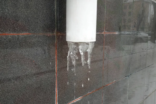 Eski evin bodrumunda bir drenaj borusu ve donmuş su var. Buzlu eski bir evin duvarında fırtına lağımı var. Soğuk şaklatma, kış.