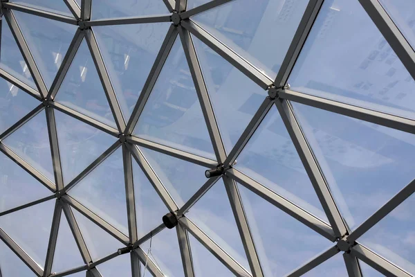 View of the sky through the glass ceiling. The complex shape of the roof canopy, created from triangular metal modules and profiles.