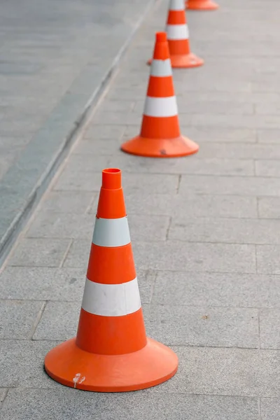 Several road cones on a square gray tile. Orange cones with white stripes. Fencing during road construction; differentiation of movement; designation of emergency sections and accident points