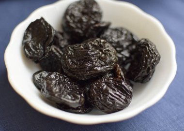 Mavi arka planda beyaz bir kasede kurumuş erik.