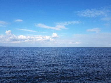 Koyu mavi deniz ve gökyüzü bulutlarda. Beyaz bulutlu parlak mavi gökyüzü ve deniz arka planındaki suyun parlayan yüzeyi..